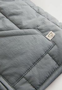 Grau gesteppte Decke mit einer weichen, strukturierten Oberfläche. Verfügt über ein kleines Bärchenetikett und kantige Stickdetails.