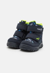 Stivali per bambini blu navy con una tomaia in tessuto testurizzato, caratterizzati da dettagli verdi, cinturini in Velcro e un design decorato in blu e verde.