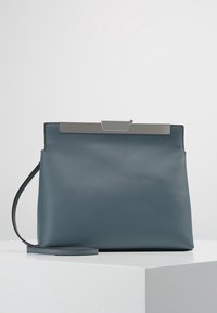 Blå läderhandväska med en elegant, strukturerad design. Har ett silverfärgat spänne och en avtagbar axelrem. Slät textur, minimala accenter.