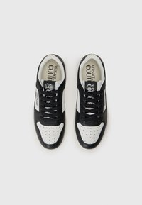 Sapatilhas em preto e branco com material em pele, bico perfurado, painéis contrastantes, atacadores planos e marcação impressa no interior.