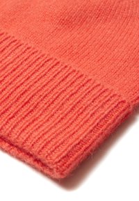 Bonnet en tricot de couleur corail avec une texture côtelée, présentant un aspect doux et duveteux, et un revers au bord inférieur.