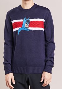 Marineblauwe trui van gebreid materiaal met een opvallende Batman-afbeelding, verfraaid met rode en witte horizontale strepen over de borst.