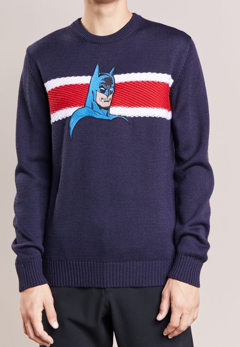 Marineblauwe trui van gebreid materiaal met een opvallende Batman-afbeelding, verfraaid met rode en witte horizontale strepen over de borst.