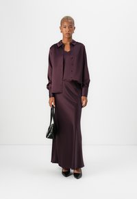 Burgundy satin blouse with buttons, paired with a matching satin skirt. Black handbag and pointed-toe heels complete the look.