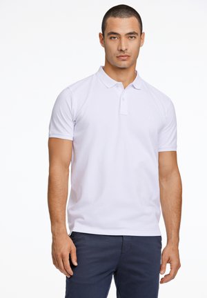 Camisa polo blanca con cuello clásico y dos botones, de manga corta y corte ajustado, combinada con pantalones azul marino. Diseño minimalista.