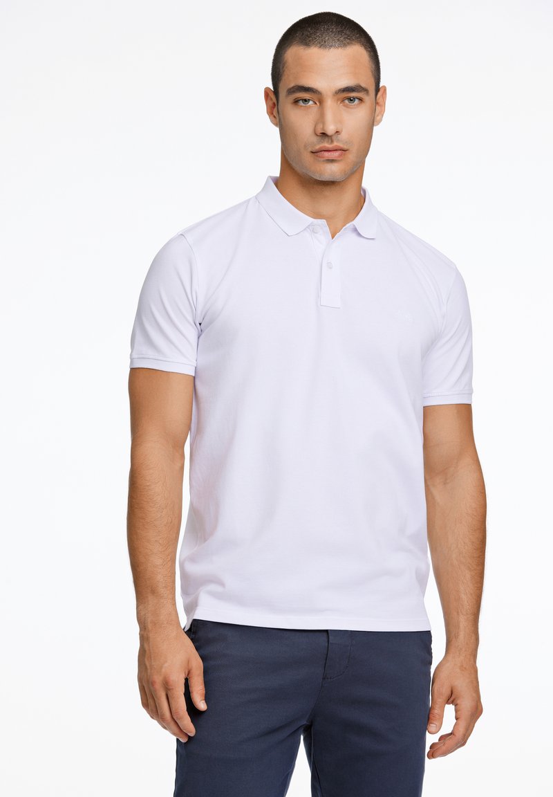 Polo bianca con colletto classico e due bottoni, maniche corte e vestibilità slim, abbinata a pantaloni blu navy. Design minimalista.