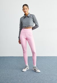 Grå avkortet hettegenser med blondekant, kombinert med høy-hvitt rosa leggings. Modellen har på seg grå og hvite sneakers, og presenterer et sporty utseende.
