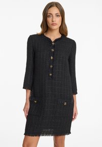 Zwarte tweed jurk met een ronde halslijn, driekwart mouwen, knopen aan de voorkant, een franjerand en twee opgestikte zakken met gouden accenten.