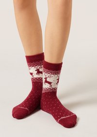 Red socks made of knitted material with white reindeer and snowflake patterns, featuring a ribbed cuff and decorative polka dots.