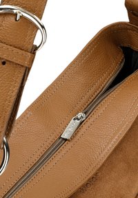 Tan leren handtas met een ritssluiting, textuur en een zilveren ritssluiting met gegraveerd merk. Accentdetails zijn een afneembare schouderband.