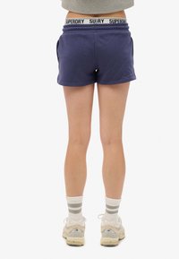 Marineblauwe shorts met een elastische tailleband, voorzien van het "SUPERDRY" logo. Ontworpen met zijzakken en een relaxed fit.