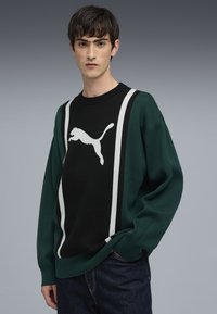 Grüner und schwarzer gestrickter Sweatshirt mit einem weißen springenden Puma-Logo und zwei vertikalen weißen Streifen. Gerippter Halsausschnitt und Bündchen.