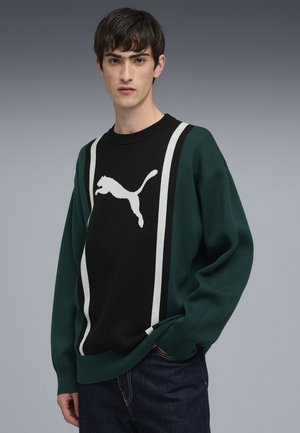 Grön och svart stickad sweatshirt med en vit hoppande Puma-logotyp och två vertikala vita ränder. Ribbad halsringning och manschetter.
