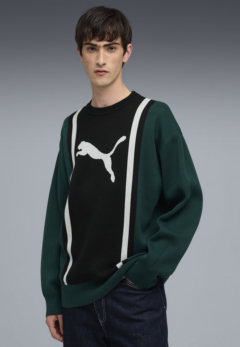 Grüner und schwarzer gestrickter Sweatshirt mit einem weißen springenden Puma-Logo und zwei vertikalen weißen Streifen. Gerippter Halsausschnitt und Bündchen.