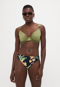 Grønn bikinioverdel med strukturerte kopper og dekorative stropper. Høytlivs underdel har en marineblå bunn med tropisk blomstertrykk i oransje og grønt.