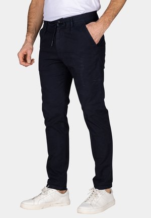 Marineblauwe katoenmix broek met een taps toelopende fit, elastische tailleband, trekkoorddetail en zijzakken, gedragen met witte sneakers.