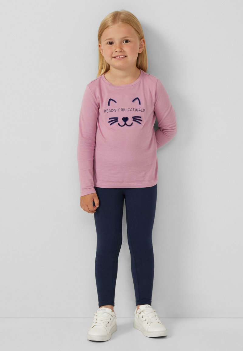 Maglietta a maniche lunghe rosa con grafica di un volto di gatto, abbinata a leggings blu scuro e sneakers bianche. Design semplice, vestibilità casual per bambini.