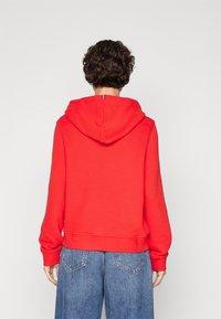 Sudadera de algodón roja con capucha trasera, dobladillo y puños acanalados. Combinada con jeans de mezclilla azules de corte holgado, que muestran un diseño casual.