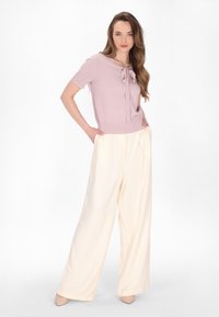 Top corto a maniche corte rosa chiaro con dettaglio a fiocco, abbinato a pantaloni larghi color crema in un tessuto morbido. Scarpe con tacco neutre.