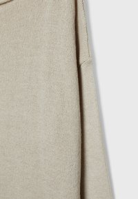 Pull en maille beige avec une coupe décontractée, un col côtelé et une texture douce. Le tissu présente un motif uniforme avec un léger éclat.