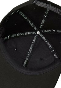 Interno della berretta nera con una texture liscia. Caratterizzata da cuciture e bande di tessuto con logo con testo in bianco e verde. Pulsante circolare sulla parte superiore.