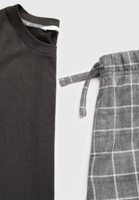 Maglione grigio scuro piegato accanto a pantaloni a quadri grigi con cordino su uno sfondo bianco.