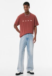 T-shirt oversize marron avec le texte blanc "Dis-moi la vérité", associé à un jean droit bleu clair et des chaussures noir et blanc.