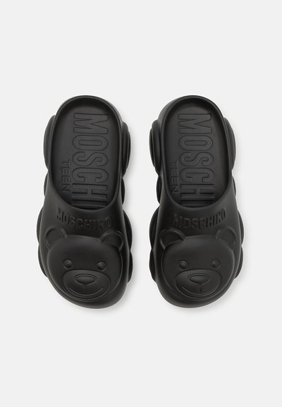 Sandalias de goma negras con un diseño de cara de oso en la parte del dedo, con "Moschino Teen" grabado en la cinta. Textura suave, forma redonda.