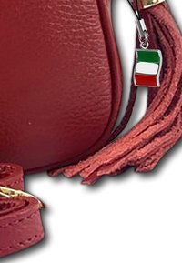 Rode leren schoudertas met een gestructureerd oppervlak, voorzien van een kwastje en een klein Italiaans vlaggetje charm dat aan een rits of riem is bevestigd.