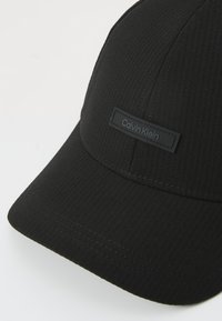 Casquette noire au design structuré, dotée d'un tissu nervuré, d'un pic arrondi et d'une étiquette avec le logo Calvin Klein à l'avant.