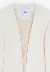 Blazer crema con solapa afilada, un bolsillo y textura suave. La etiqueta muestra "SCALPERS" con talla "S."