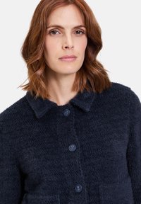 Granatowy kardigan zapinany na guziki, wykonany z teksturowanej dzianiny, z kołnierzykiem, kieszeniami frontowymi i okrągłymi guzikami.