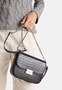 Černá crossbody taška s krokodýlím vzorem a lesklou stříbrnou sponou. Obsahuje řetízek, obdélníkový tvar a hladký povrch.