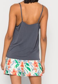 Grå spaghetti axelbands topp med lös passform, matchad med blommönstrade shorts i vitt med röda, rosa och gröna mönster.