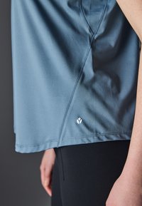 Short-sleeve, light blue athletic top made of smooth fabric, featuring a subtle logo near the hem and contoured seams for a fitted look.
