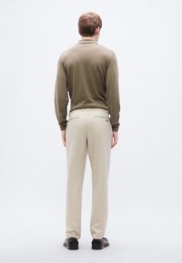 Μακρυμάνικο πουκάμισο σε ελιά πράσινο σε συνδυασμό με ανοιχτό μπεζ παντελόνι· υφή υφάσματος και εφαρμοστή σχεδίαση· λιτές λεπτομέρειες στην πίσω τσέπη.