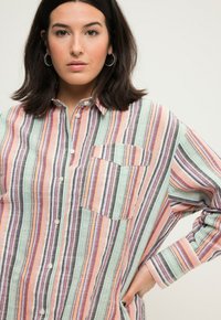 Gestreepte overhemden in pastelkleuren (roze, groen, grijs) met een borstzak, lange mouwen en een textuurstof. Verticale strepen hebben verschillende breedtes.