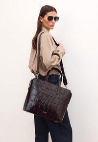 Burgundi nahkakäsite krokotiilipinnalla, kaksinkertaisilla kahvoilla ja olkahihnalla, kultaisilla varusteilla.