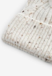 Kootud müts kreemjas-valges, tekstuursete soonte ja pruunide kiududega, pehme, villase sarnase materjaliga ning mugava istuvusega.