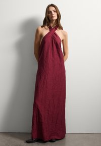 Langes, burgunderfarbenes Halterkleid mit zerknitterter Textur und überkreuztem Ausschnitt. Bodenlang, aus leichtem Material gefertigt. Einfaches Design.
