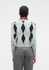 Pull en motif argyle dans des tons de gris clair, gris foncé et marine, avec une coupe ajustée et des poignets côtelés. Court au niveau de la taille. Texture douce.