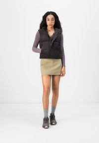 Dark gray puffer vest with a high neckline and front pockets, worn over a lavender long-sleeve top and light-colored skirt, paired with gray socks and shoes.