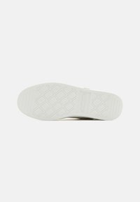 Semelle de chaussure avec une surface en caoutchouc blanc texturé, présentant un motif en diamant et un logo rectangulaire près de la zone du talon.