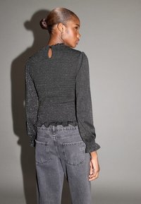 Top nero con texture, orlo arricciato e maniche lunghe, caratterizzato da una piccola apertura a goccia sul retro, abbinato a jeans grigi a vita alta.