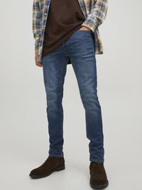 Slim-fit blue jeans made of denim, featuring a classic five-pocket design. Worn with a brown t-shirt and a plaid shirt layered over.