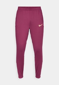 Calças de atletismo bordeaux com um corte afunilado, cintura elástica e um pequeno logotipo da Nike bege na coxa esquerda. Material liso e elástico.