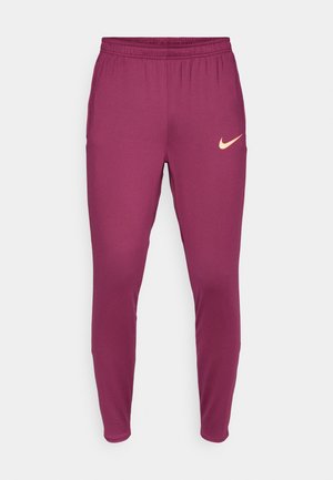 Bordowe spodnie sportowe o zwężanym kroju, z elastycznym pasem i małym beżowym logo Nike na lewym udzie. Gładki, elastyczny materiał.