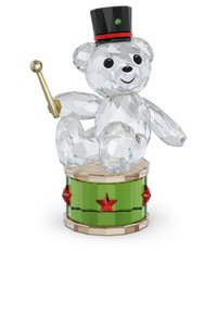 Crystalová figúrka medveďa s čiernym klobúkom, ktorý drží zlatý dáždnik, sediaci na zelenej bubnovanej s červenými hviezdami a drevenými akcentmi.