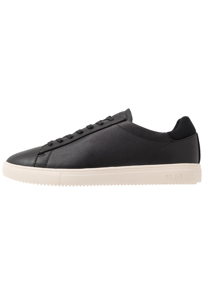 Basket basse en cuir noir avec des lacets noirs et une semelle en caoutchouc blanche, vue de la face extérieure.