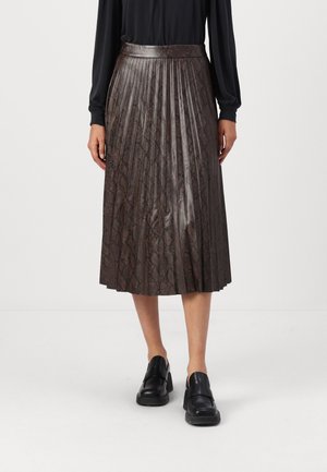 Jupe midi plissée marron avec un imprimé serpent subtil portée avec un top noir à manches longues et des mocassins noirs épais sur un fond uni.